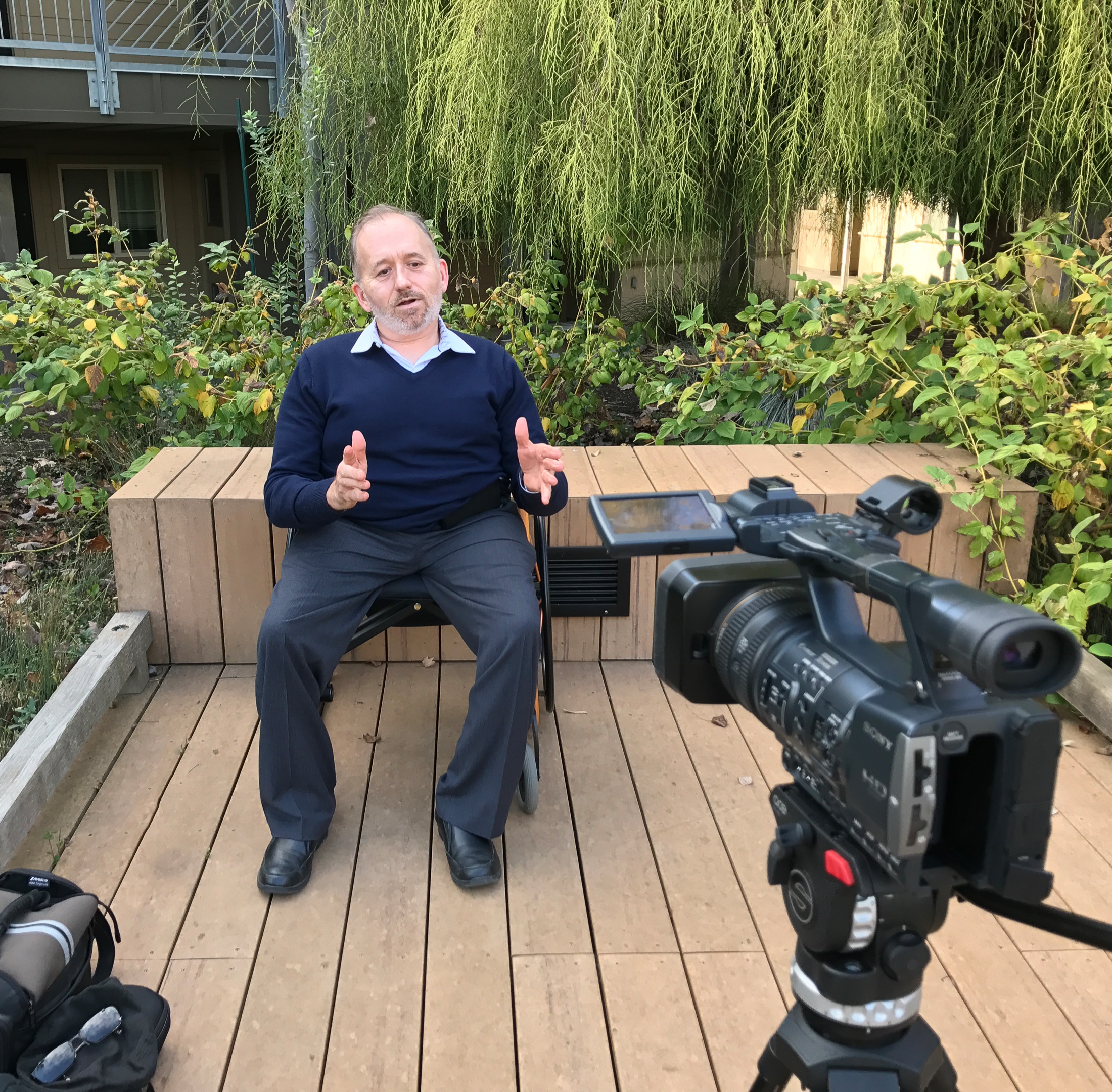 Erick speaking on camera outdoors, hands mid-gesture