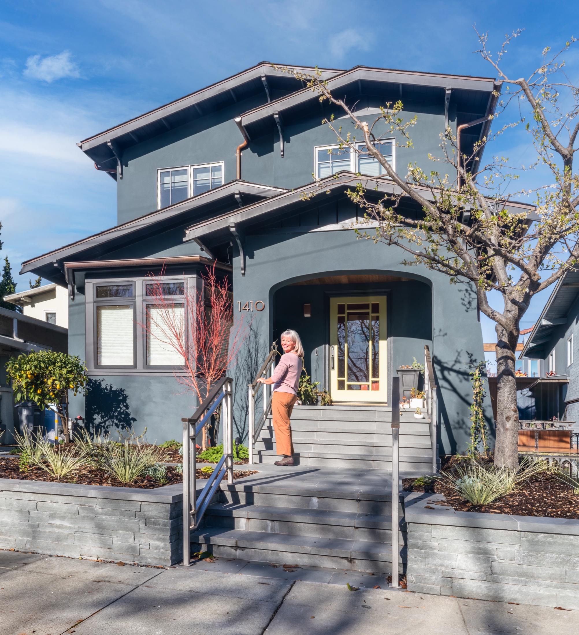 A woman smiling as she uses a handrail to walk up the front steps of a beautiful craftsman home